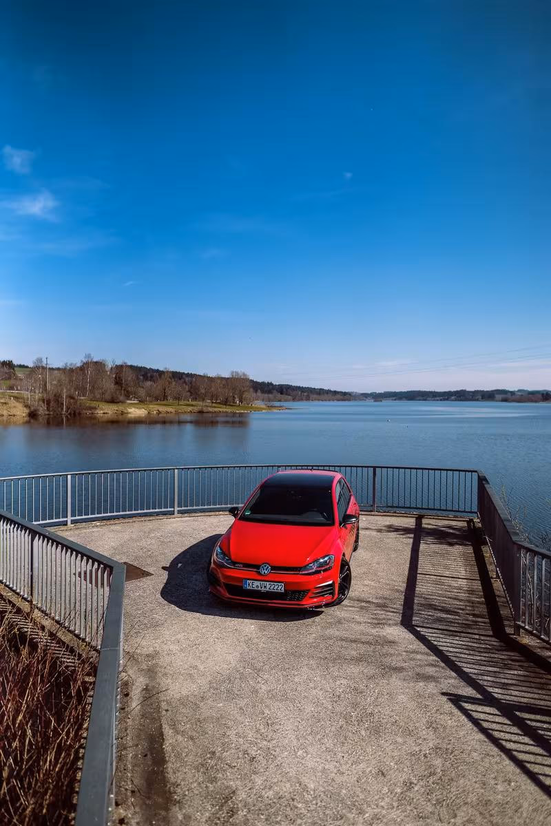 Volkswagen: Roter VW Golf GTI auf einer Sonnenterrasse vor einem See