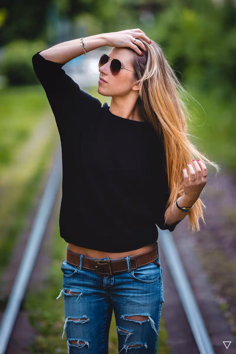 Lifestyle: Frau mit Sonnenbrille in Schwarz und Jeans auf einer Bahnstrecke.