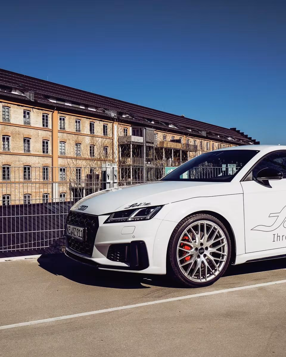 Weißer Audi RS 7 mit „White Widow“-Grafik vor historischer Fabrikhalle.