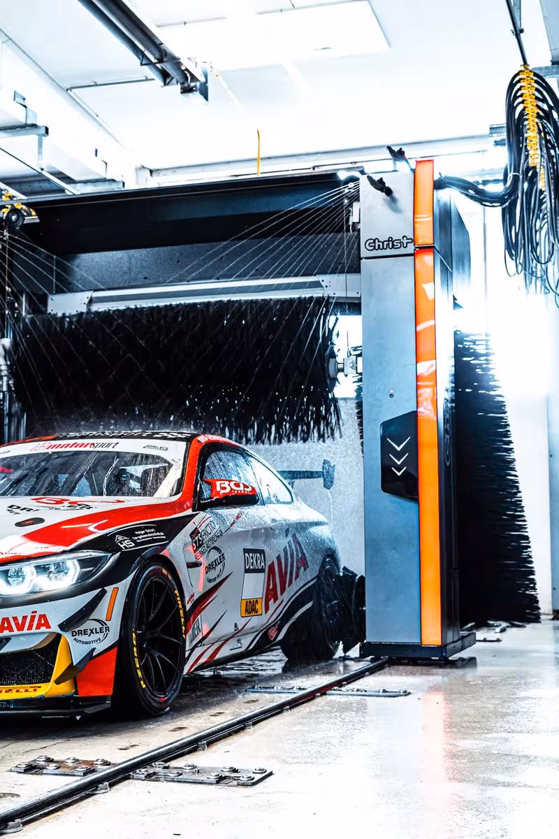 Rennwagen mit Sponsorenlogos wird in einer Christ AG Hochdruck-Waschanlage gereinigt.