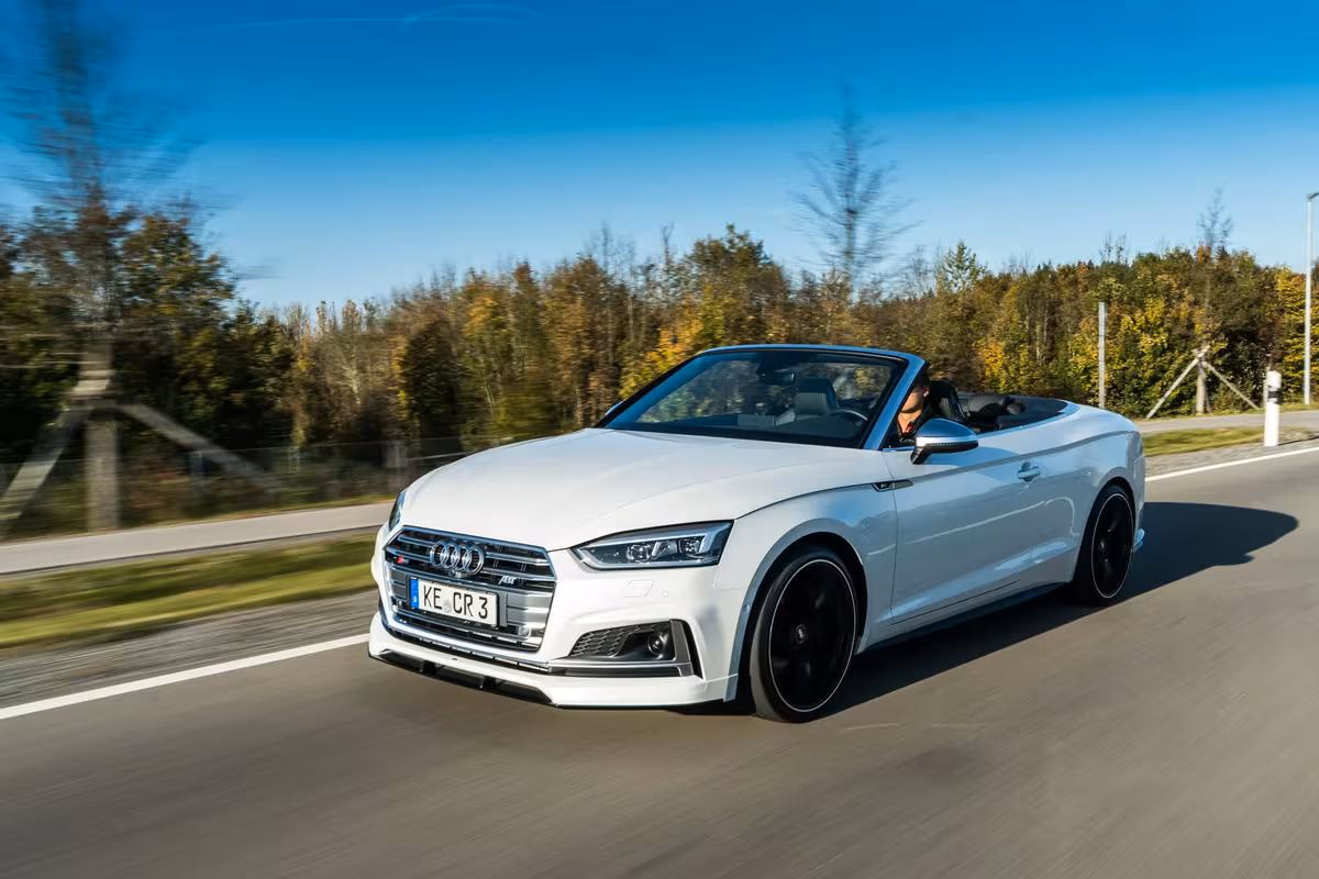 Weißer Audi A5 Cabriolet fährt auf einer Landstraße durch eine herbstliche Landschaft.