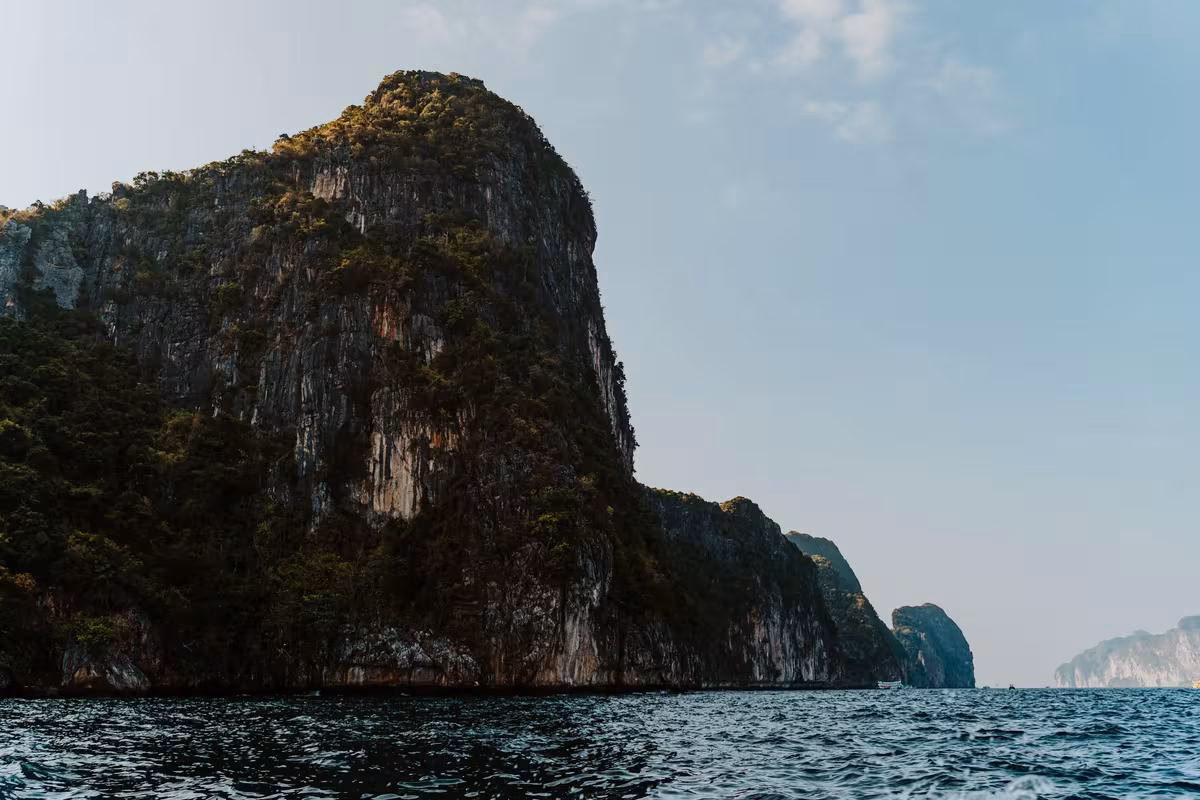 Thailand: Steile, bewaldete Felsklippe, die steil aus dem Meer aufragt.