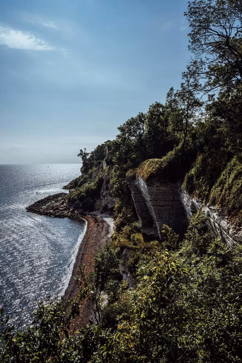 Copenhagen: Steile, bewachsene Klippe über einem glitzernden Meer mit Strand und Felsen.