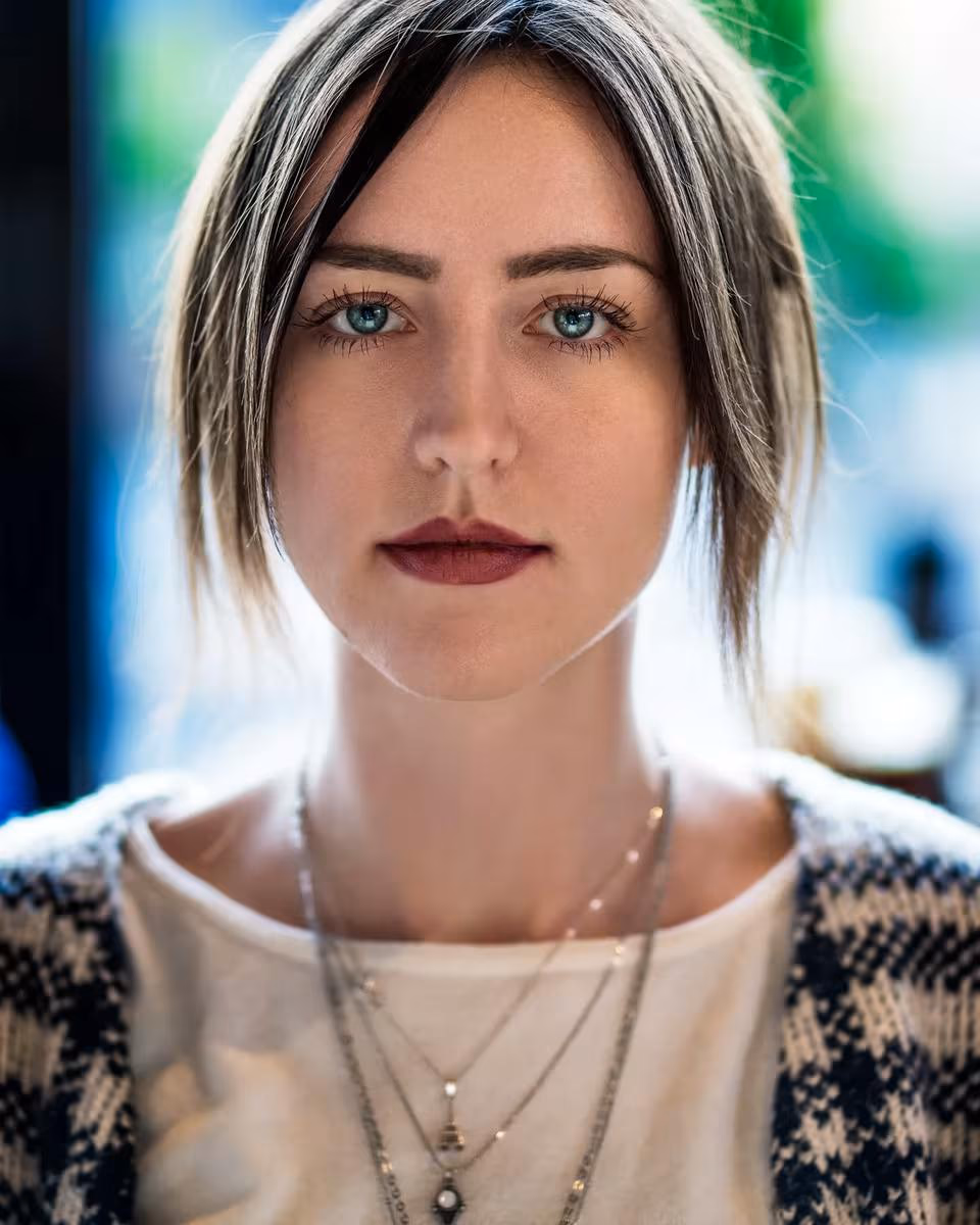 Lifestyle: Porträt einer Frau mit kurzem Haar und mehreren Halsketten vor unscharfem Hintergrund.