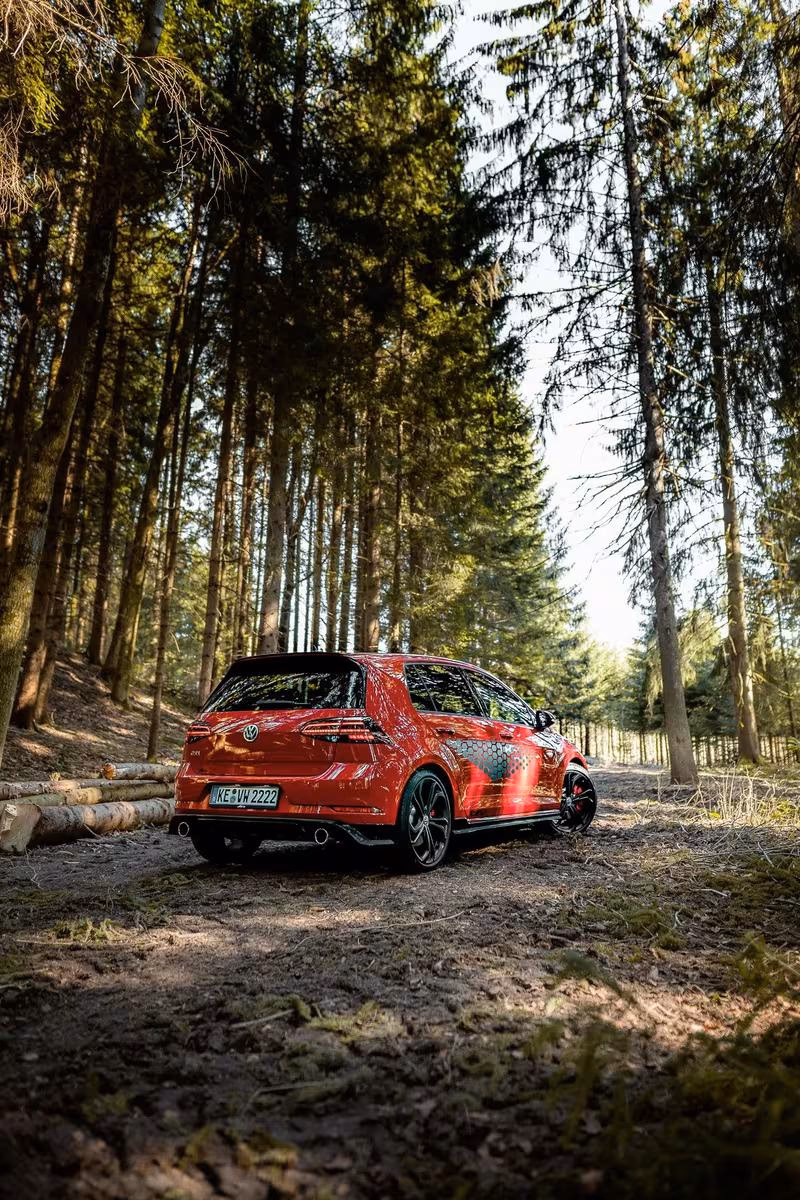 Volkswagen: Roter VW Golf GTI mit Sonderlackierung auf einem Waldweg.