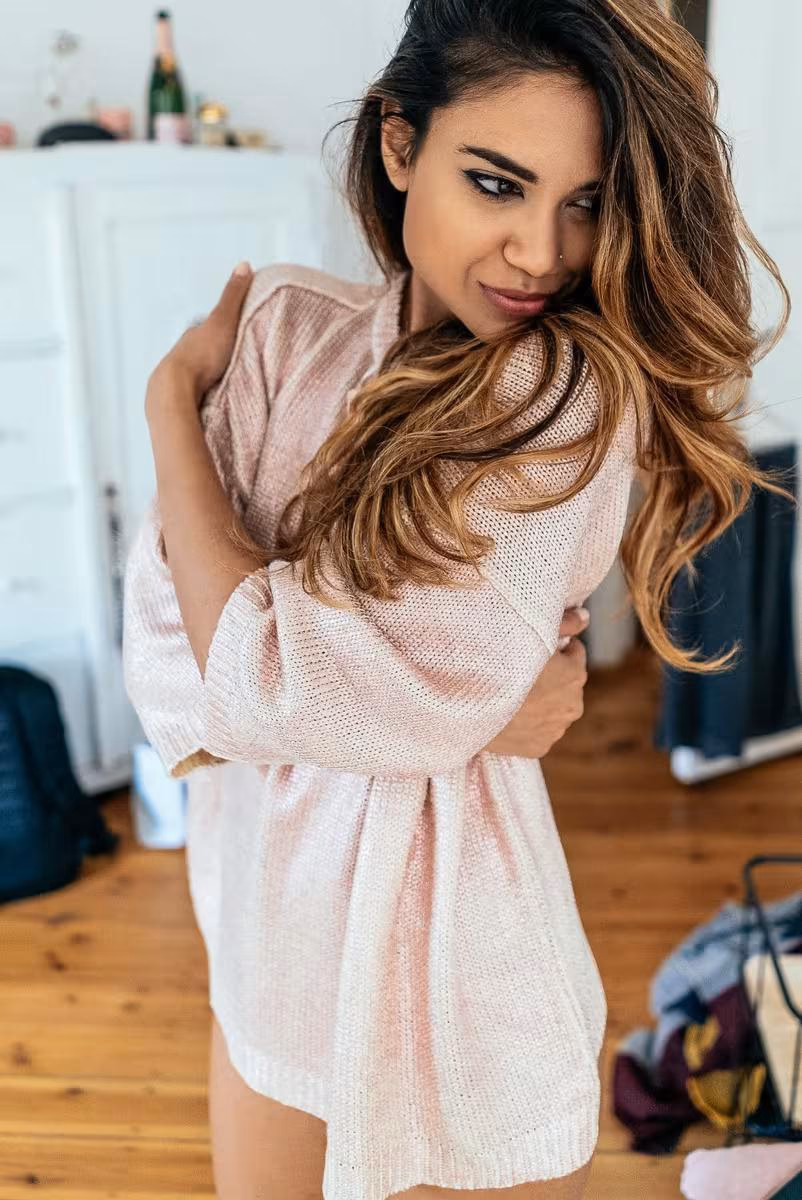 Lifestyle: Frau in rosa Strickkleid mit verschränkten Armen in hellem Raum