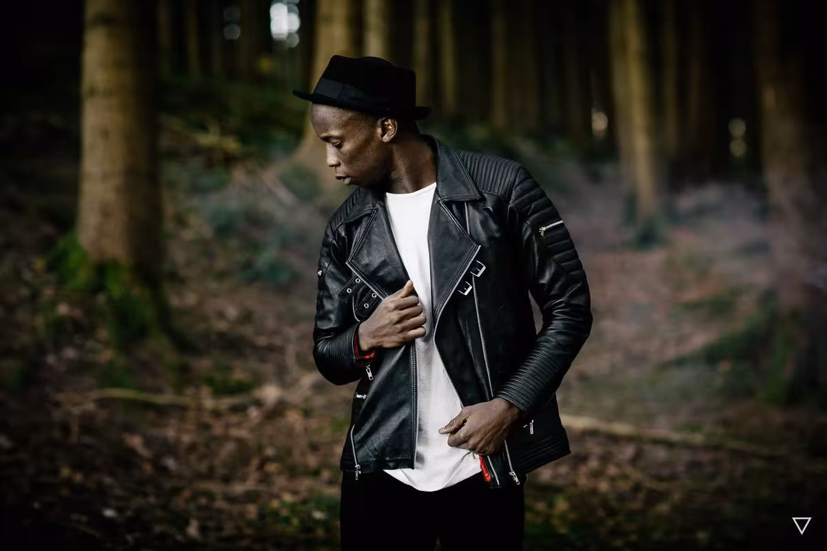 Lifestyle: Mann in Lederjacke und Hut, der im dunklen Wald steht.