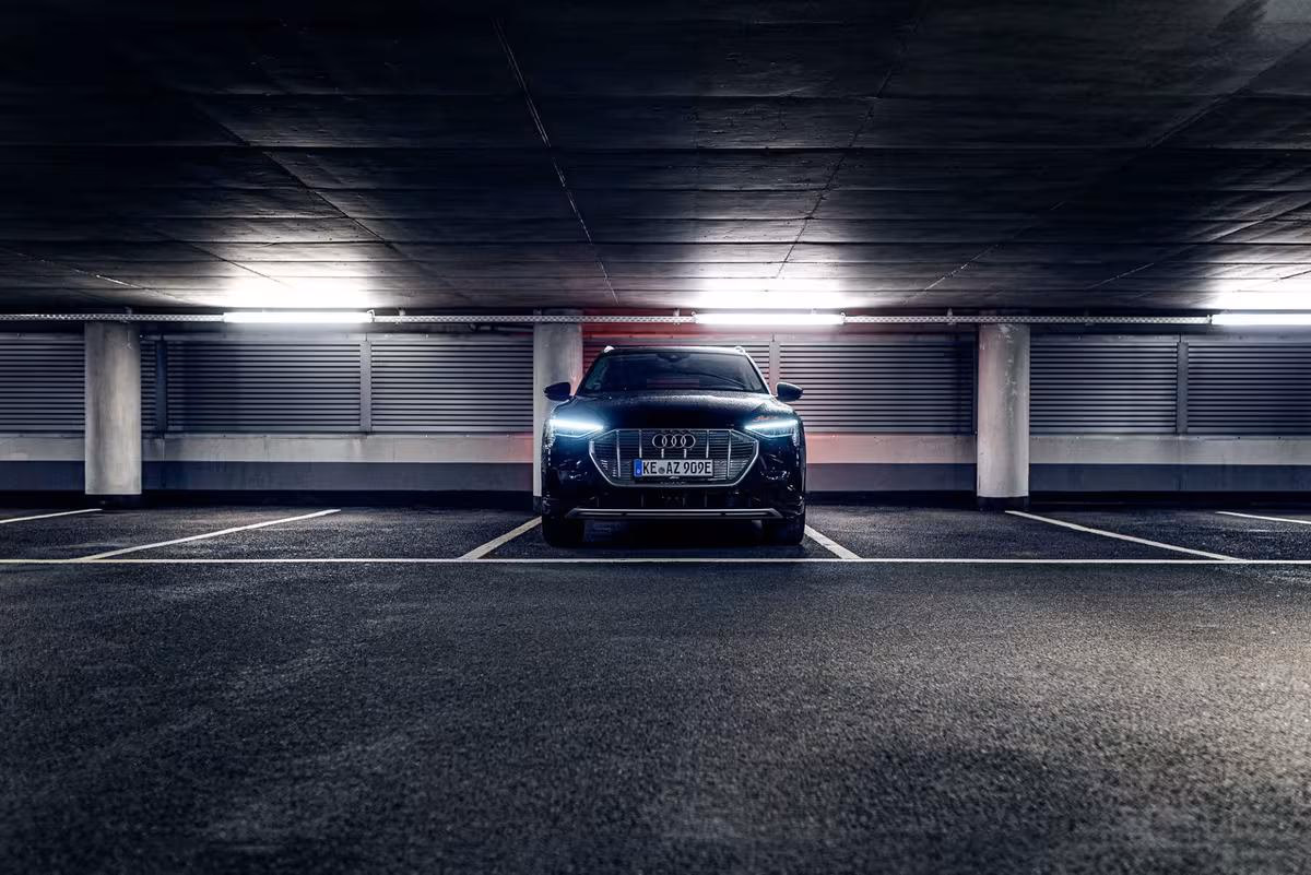 Black Audi e-tron with illuminated LED headlights parked in a dark underground garage.