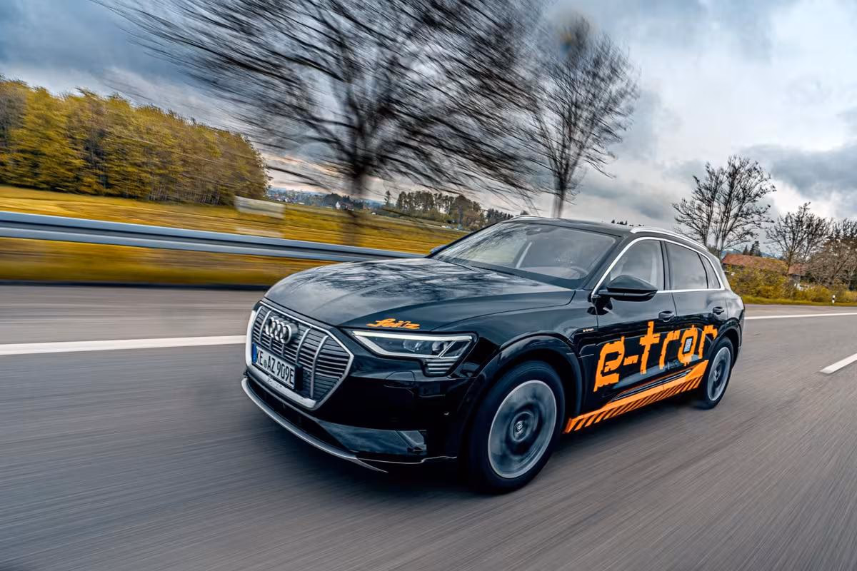 Black Audi e-tron with orange lettering driving fast on a country road.