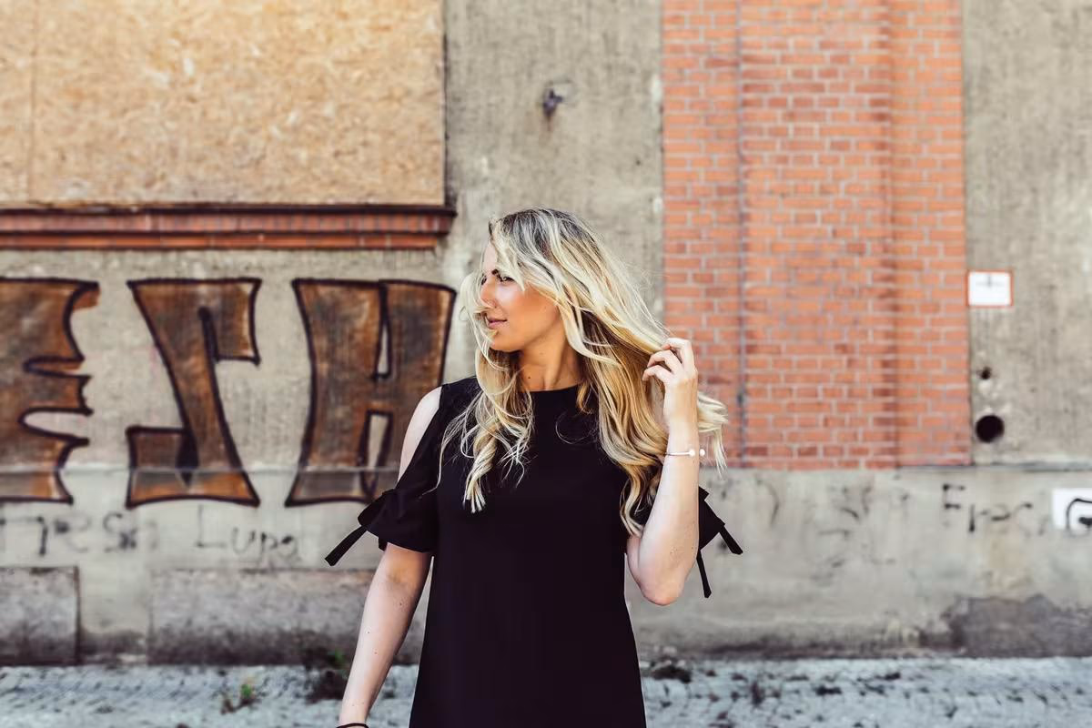 Lifestyle: Blonde Frau in schwarzem Kleid vor einer Wand mit Graffiti.
