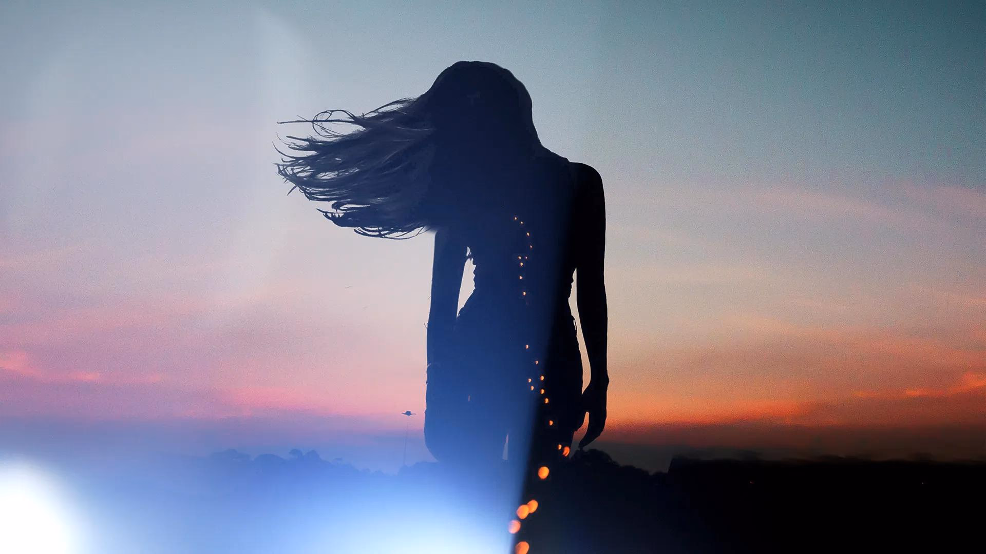 Silhouette einer Frau mit wehendem Haar vor einem bunten Sonnenuntergang.
