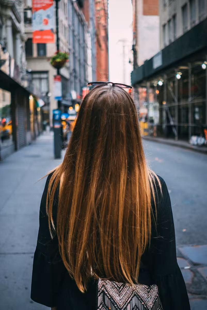 Lifestyle: Frau mit langen Haaren und Sonnenbrille auf dem Kopf, von hinten auf einer Stadtstraße.