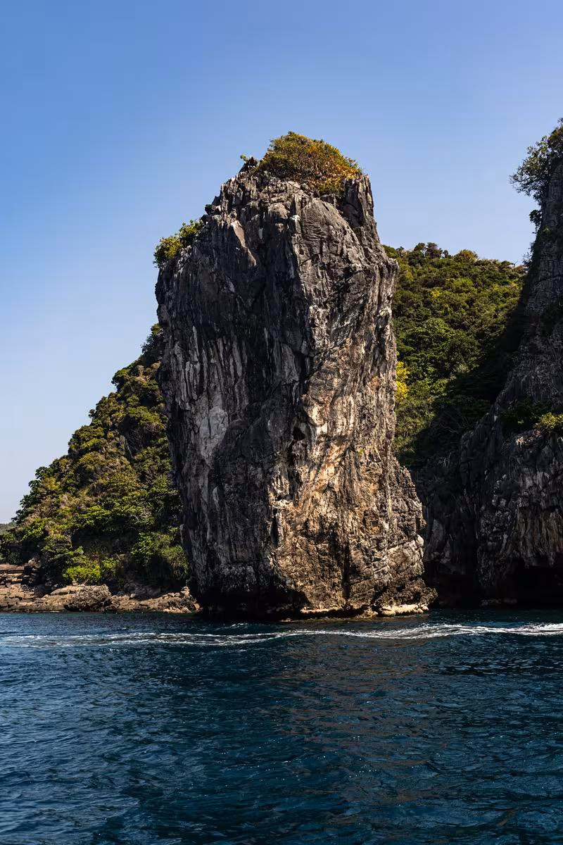 Thailand: Steile Felsformation mit Vegetation am Meer unter blauem Himmel
