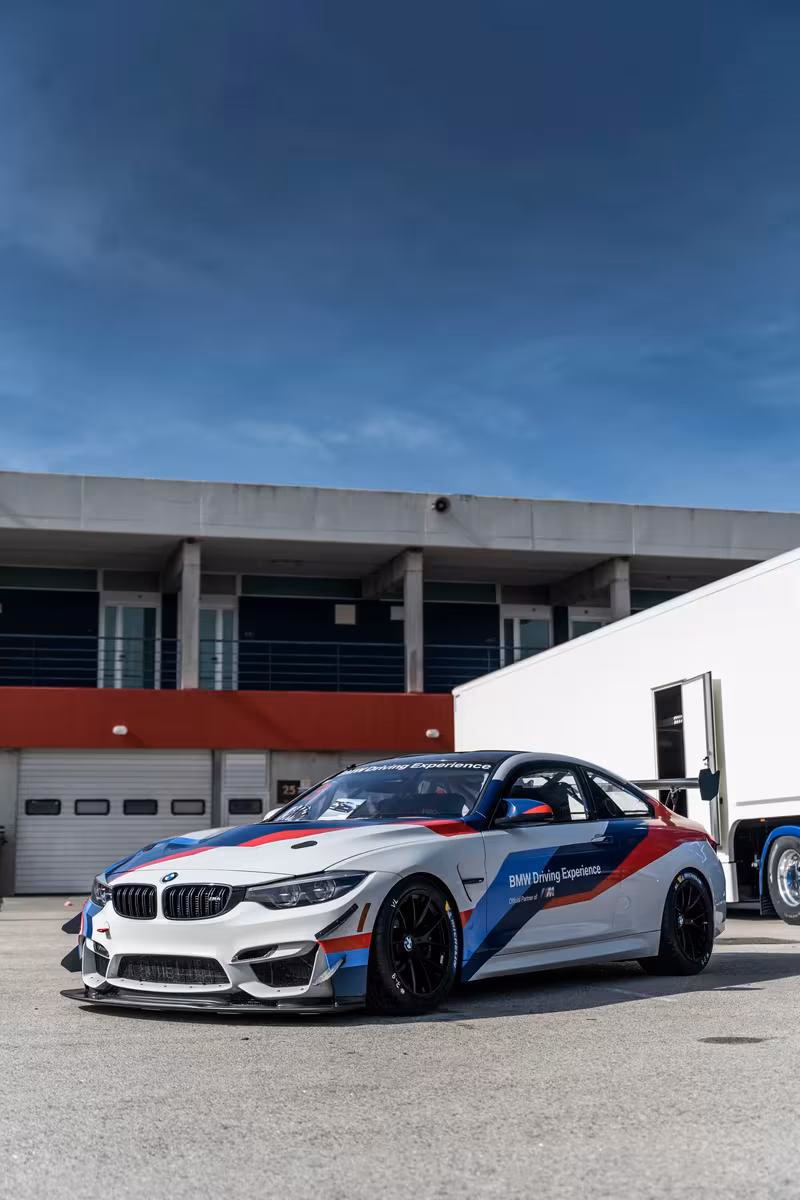 BMW M4 Coupé mit BMW Driving Experience Lackierung vor einer Motorsport-Garage.