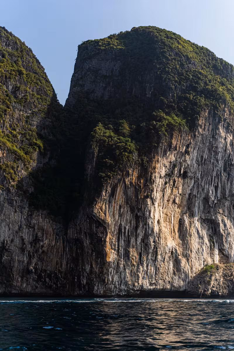 Thailand: Steile, bewachsene Felsklippe, die direkt ins Meer ragt.