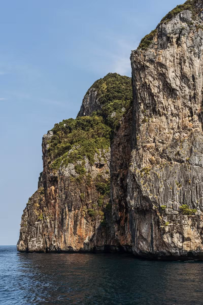 Thailand: Steile, bewachsene Felsklippe, die direkt ins Meer ragt.