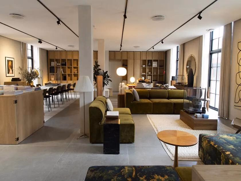 Axor: Helle Galerie mit grünen Sofas, Holzmöbeln, Regalen und großen Fenstern.