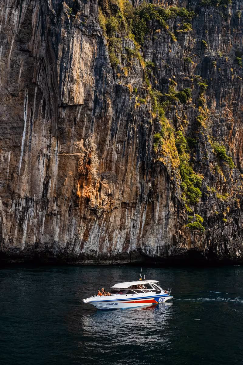 Thailand: Motorboot mit Passagieren vor einer steilen, bewachsenen Felswand im Wasser.