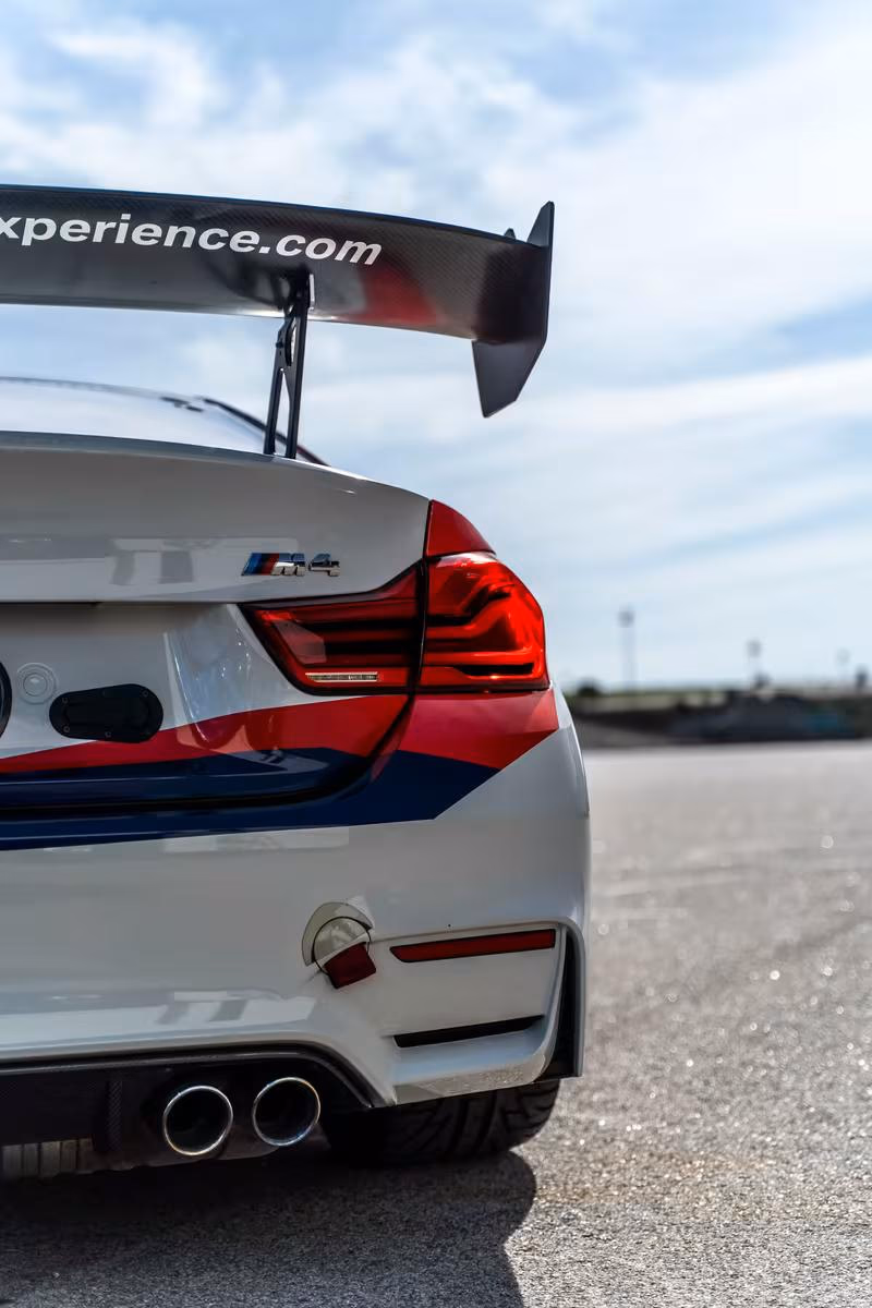 BMW M4 mit großem Carbon-Spoiler und Aufdruck „experience.com“ auf der Rennstrecke.