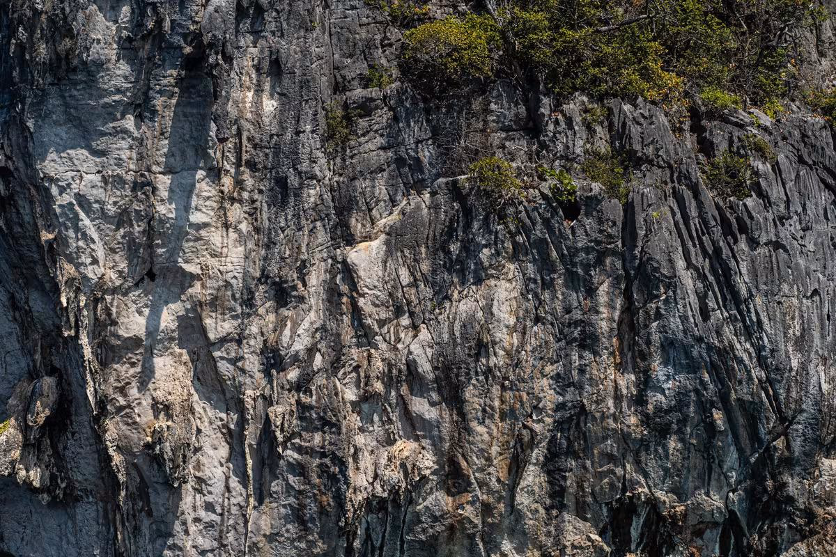 Thailand: Steile Felswand mit spärlichem Bewuchs und markanten Schatten