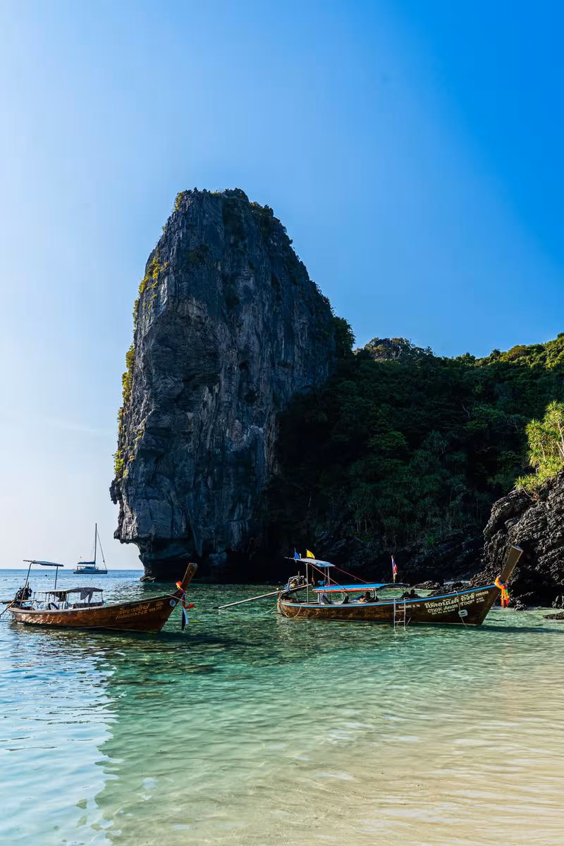 Thailand: Zwei thailändische Longtail-Boote vor einer steilen Kalksteinfelsformation im türkisfarbenen Meer.