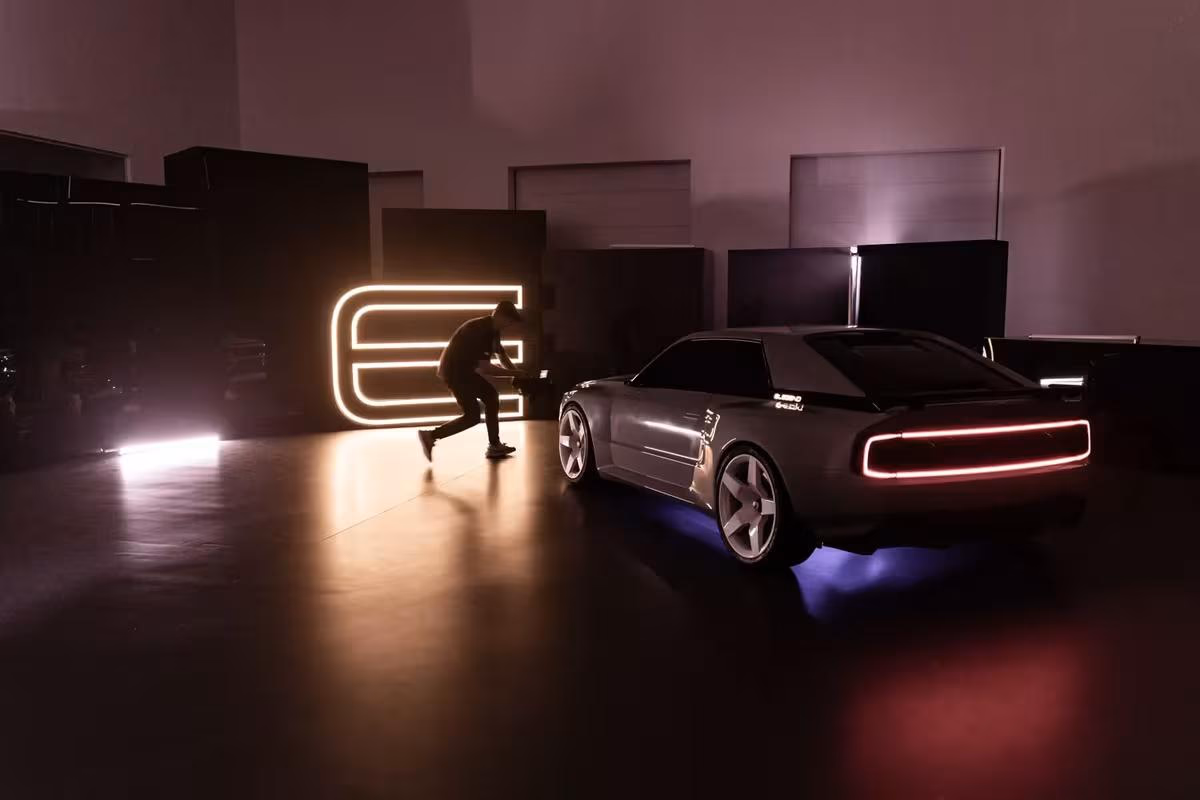 Silhouettierter Mann neben silbernem E-Legend-Prototyp und leuchtendem Neon-Logo in dunkler Halle.