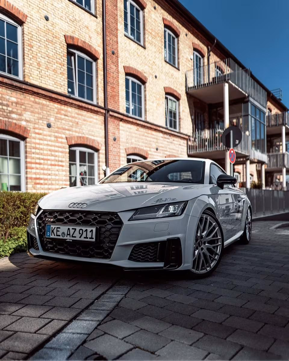 Silberner Audi TT S vor rotem Backsteinhaus auf Kopfsteinpflaster.