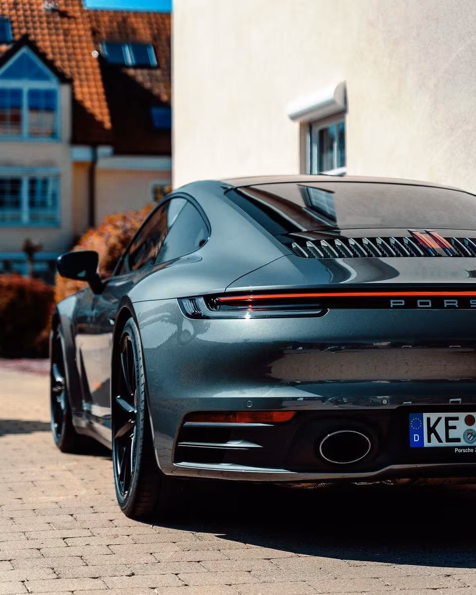 Grauer Porsche 911 Carrera 4S von hinten auf Kopfsteinpflaster vor einem Haus.