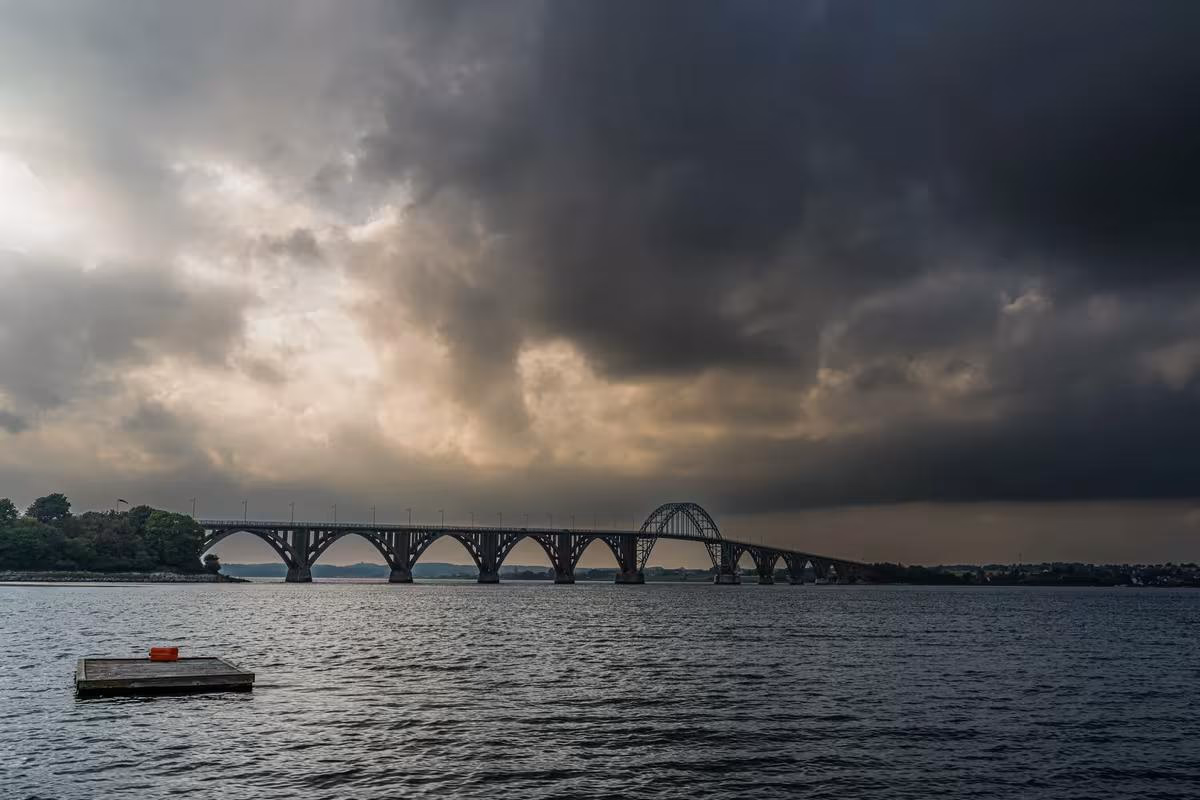 Copenhagen: Bogenbrücke über breites Gewässer bei dramatischem, bewölktem Himmel.