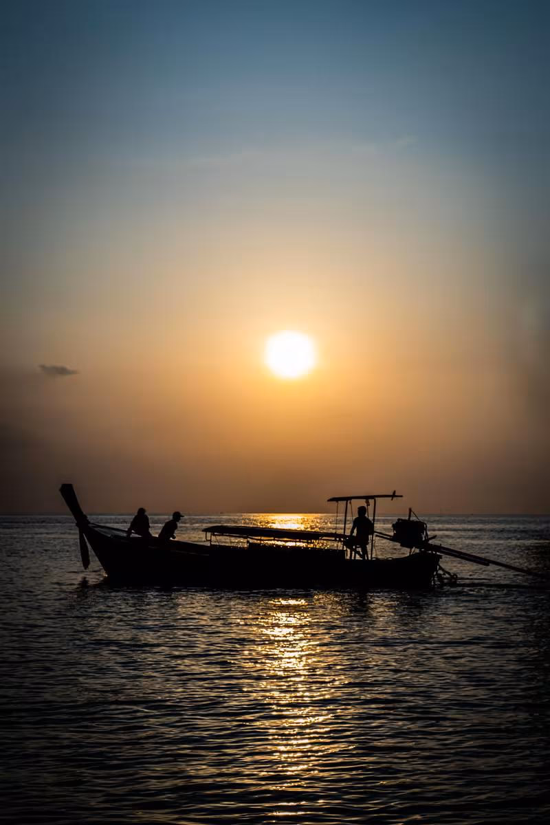 Thailand: Silhouette eines Fischerboots mit drei Personen vor sonnenuntergehender See