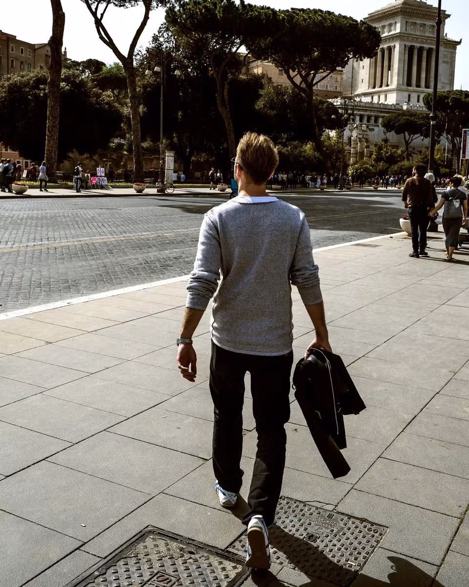 Lifestyle: Mann mit Sakko in der Hand geht auf einem Platz in Rom.