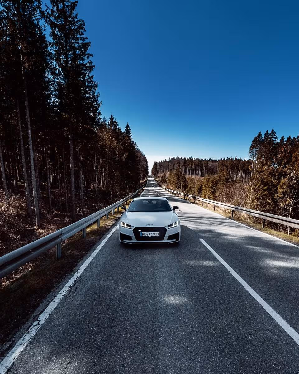 Weißer Audi RS 7 fährt auf einer geraden Waldstraße im Allgäu.