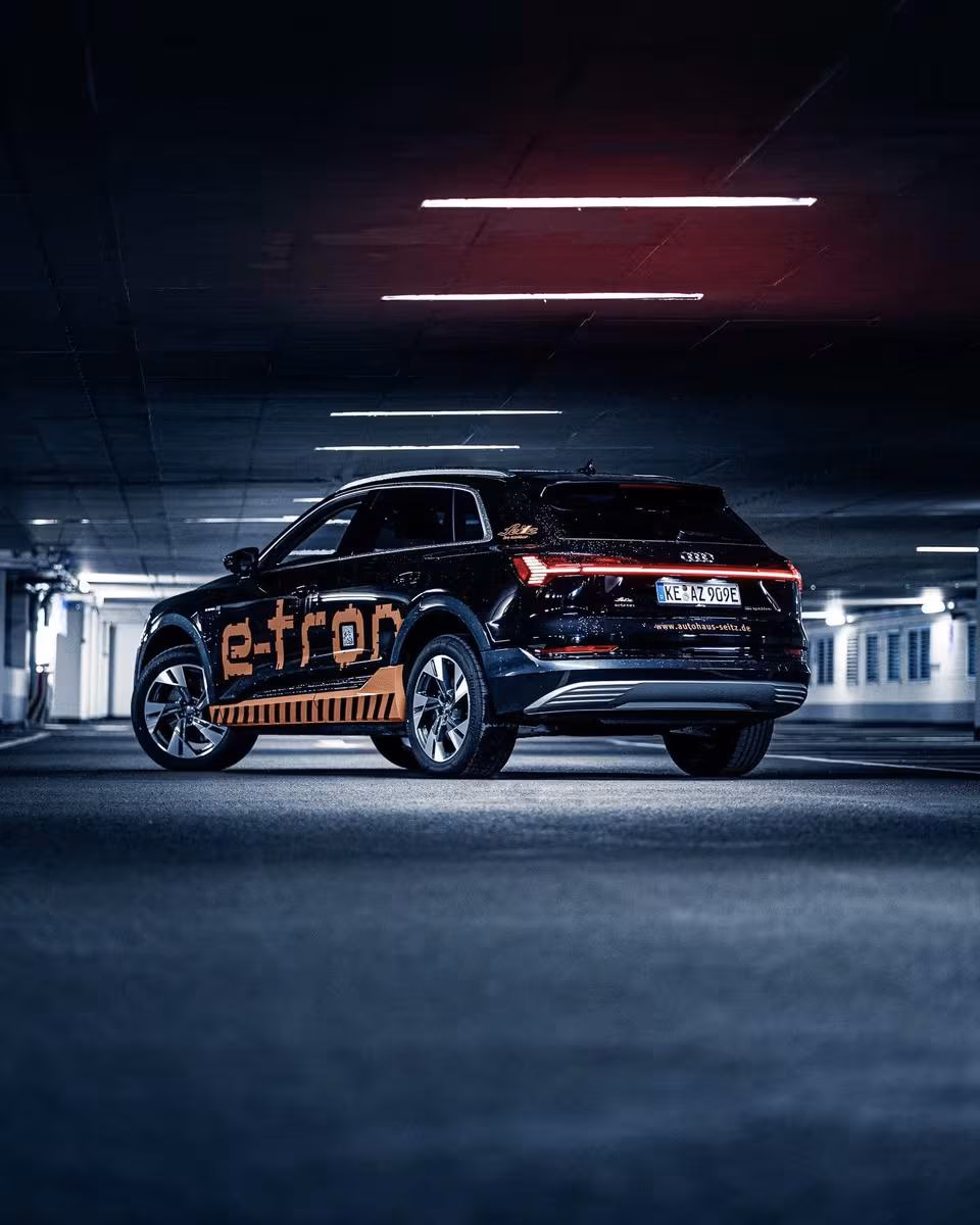 Black Audi e-tron with orange vinyl wrap in a parking garage.
