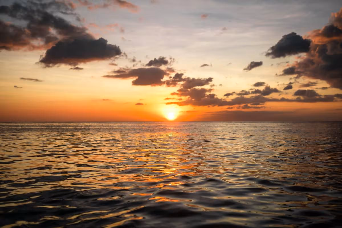 Thailand: Sonnenuntergang über dem Meer mit goldenem Licht und dunklen Wolken.