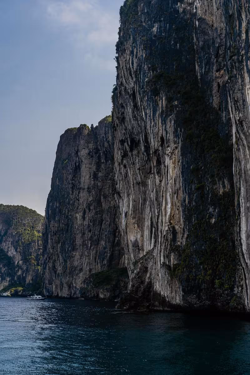 Thailand: Steile Kalkfelsenklippe am Meer mit Boot im Hintergrund