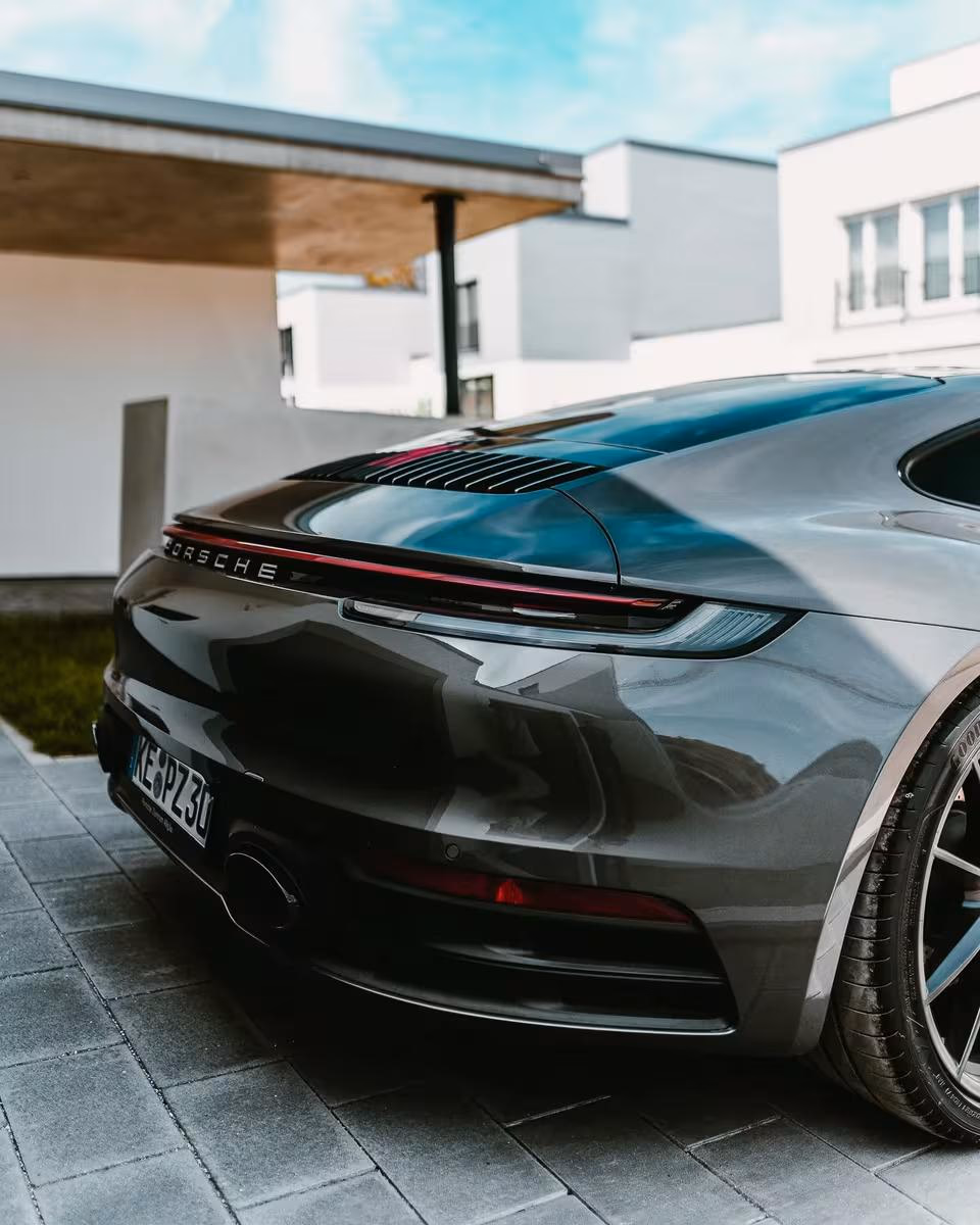 Rückansicht eines dunklen Porsche 911 Carrera 4S vor moderner Architektur.