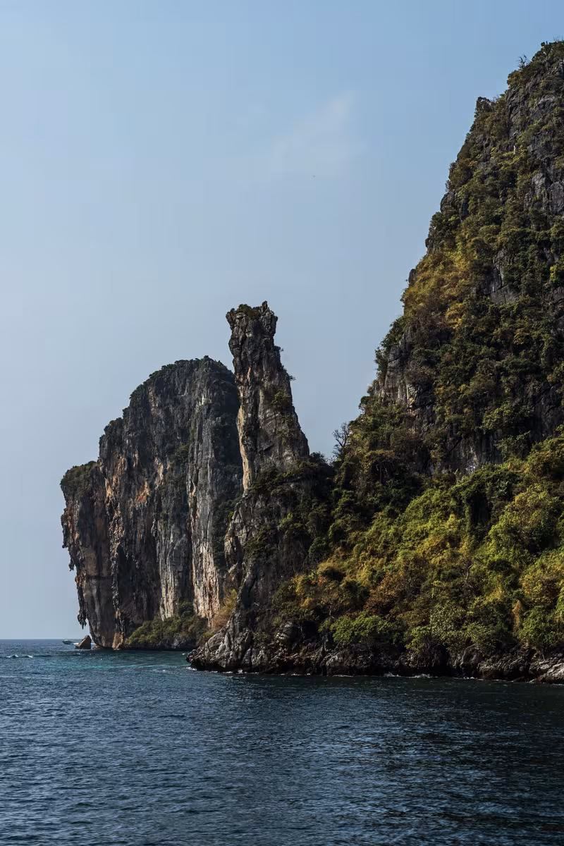 Thailand: Steile, bewachsene Felsklippen ragen aus dem Meer unter einem klaren Himmel.