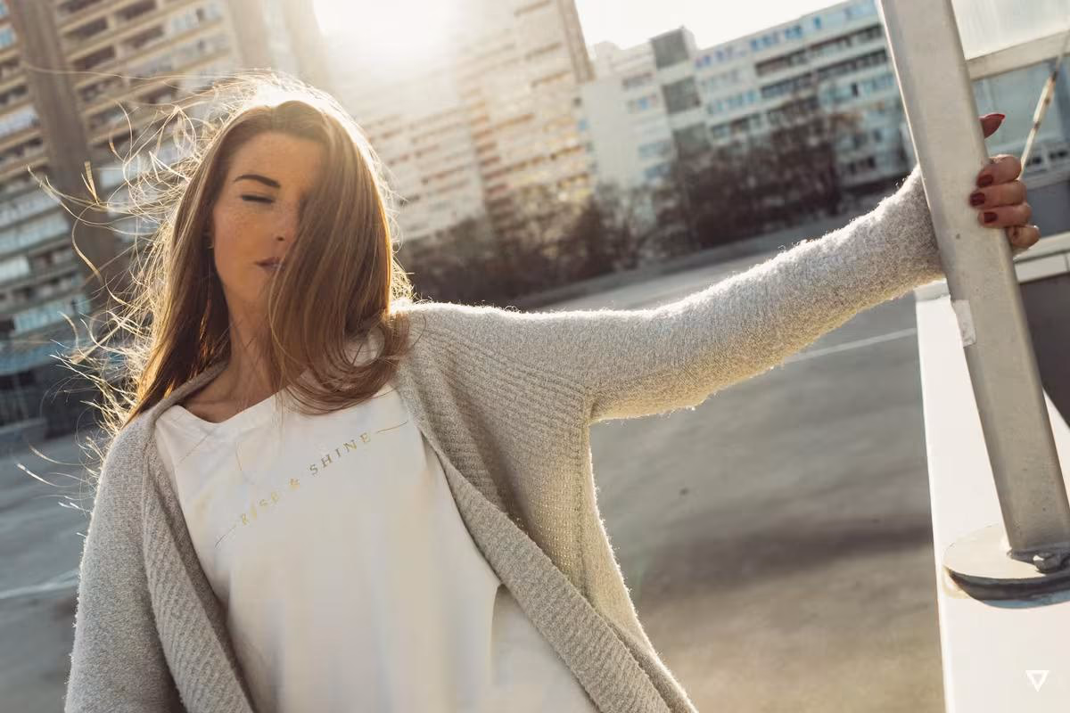 Lifestyle: Frau in weißem T-Shirt mit „Rise & Shine“-Schriftzug und grauem Cardigan im Wind