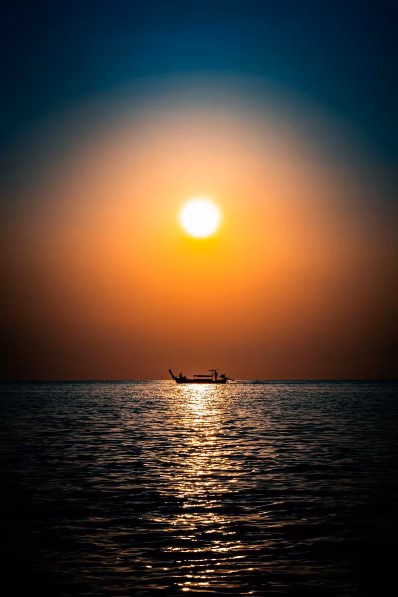 Silhouette eines Fischerboots auf dem Meer bei Sonnenuntergang in Thailand.