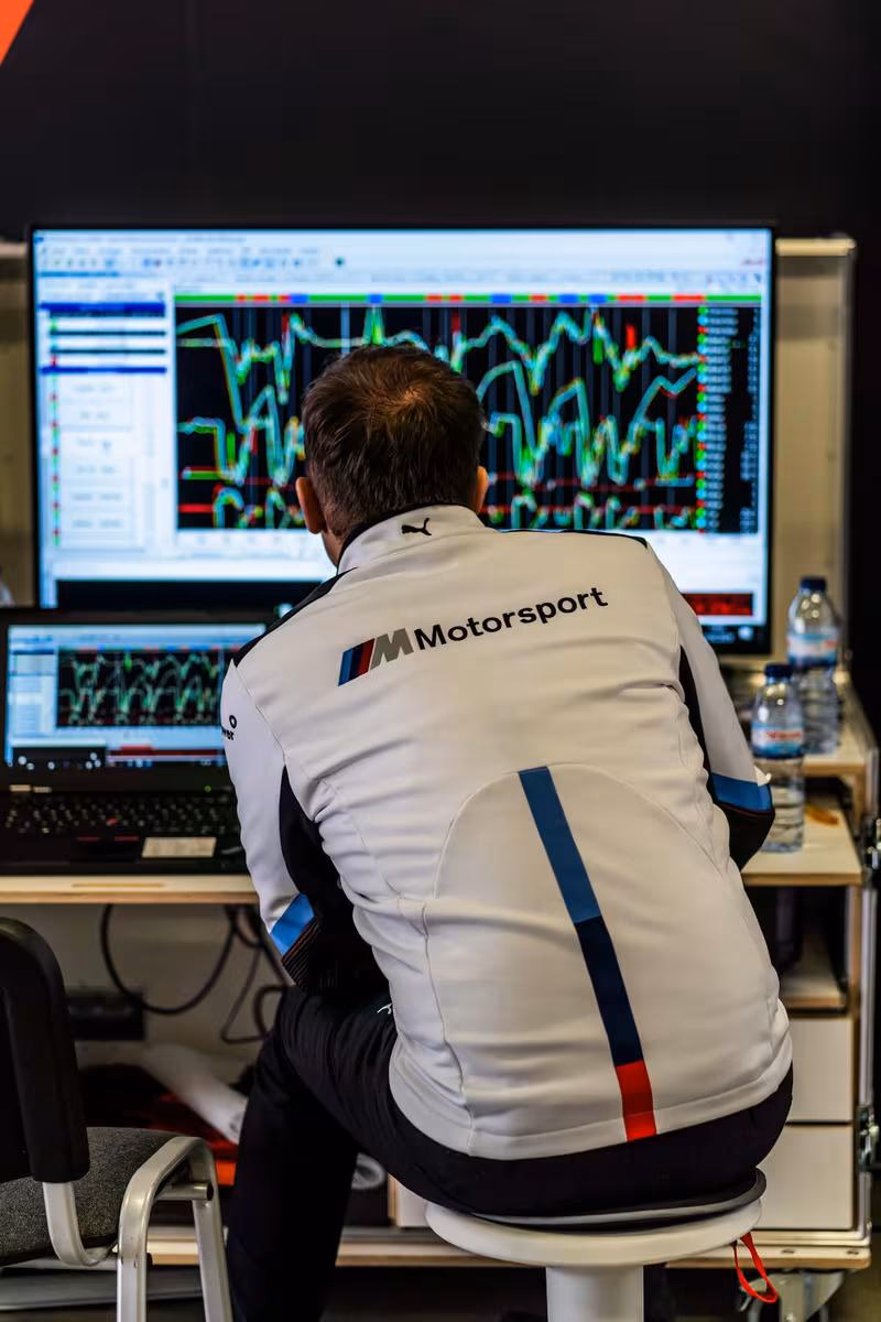 Mann in BMW-Motorsport-Jacke analysiert Telemetrie-Daten an zwei Bildschirmen.