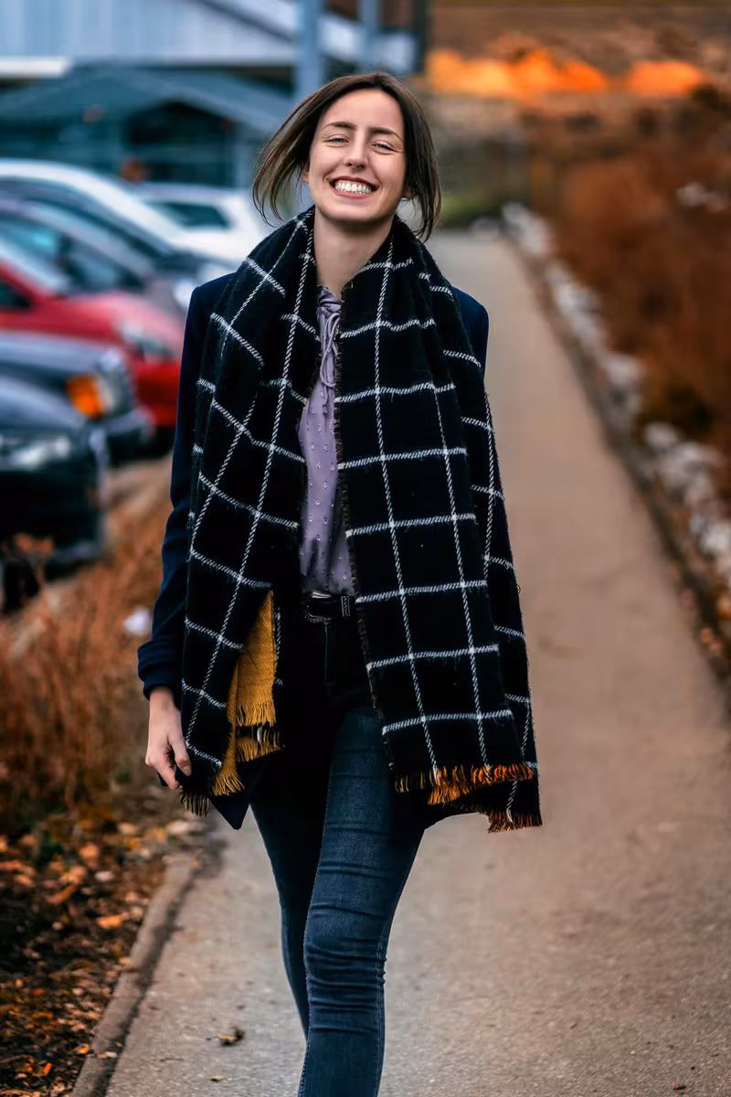 Lifestyle: Lachende Frau mit kariertem Schal und Jeans auf einem Weg.