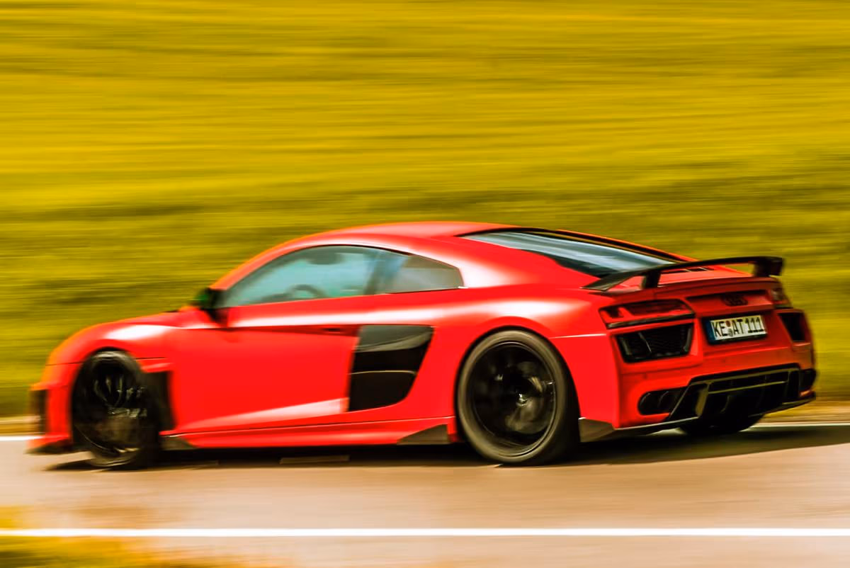 Audi: Rotes Sportauto mit Heckspoiler fährt bei hoher Geschwindigkeit über eine Straße.