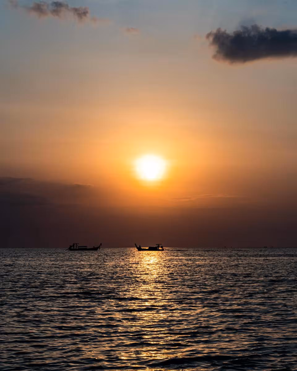Thailand: Sonnenaufgang über dem Meer mit zwei Booten im Hintergrund