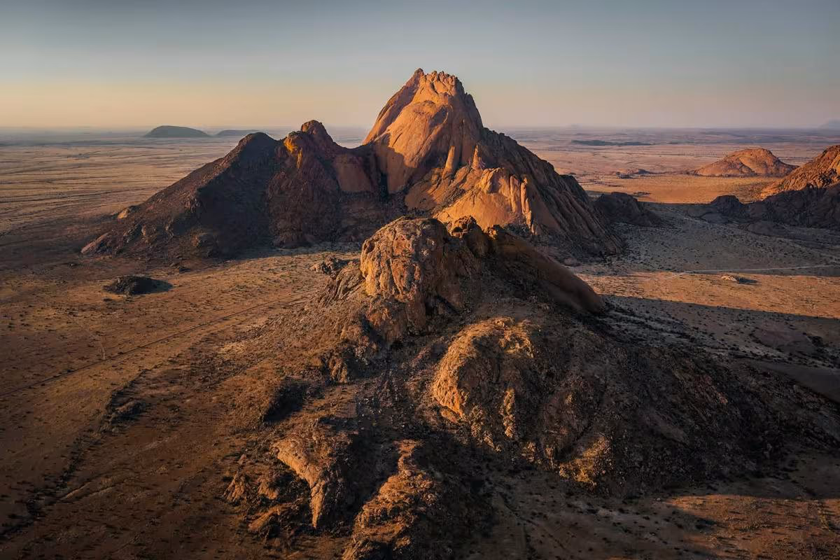 Fujifilm: Luftaufnahme einer felsigen Bergformation in einer weiten Wüstenlandschaft bei Sonnenuntergang.
