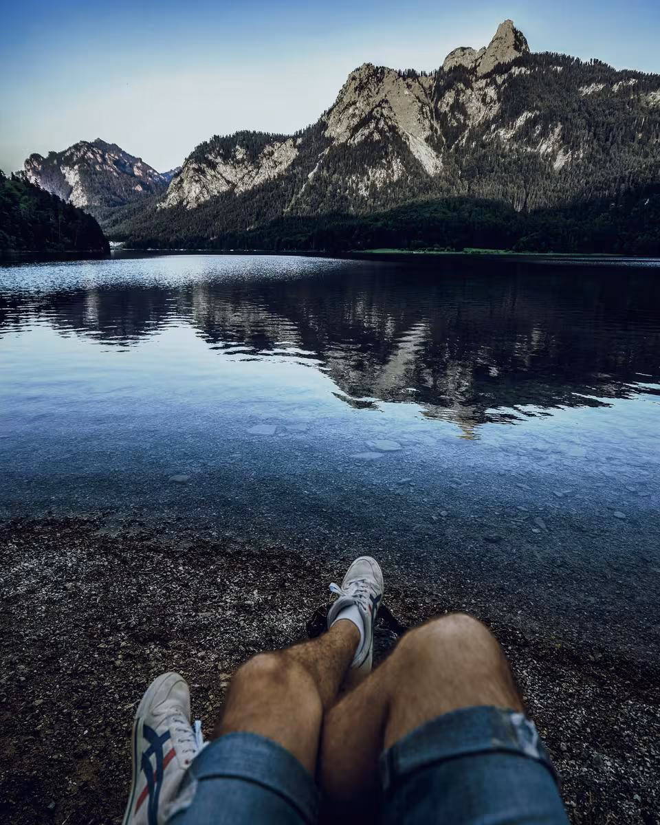 Lifestyle: Beine in Sneakern am Ufer eines Bergsees mit Bergspiegelung