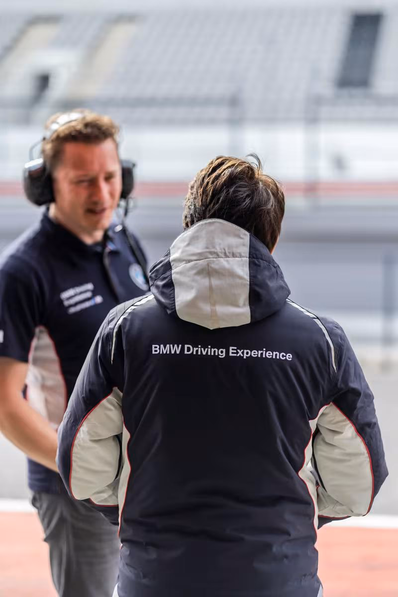 Zwei Männer auf einer Rennstrecke, einer trägt eine BMW Driving Experience Jacke.