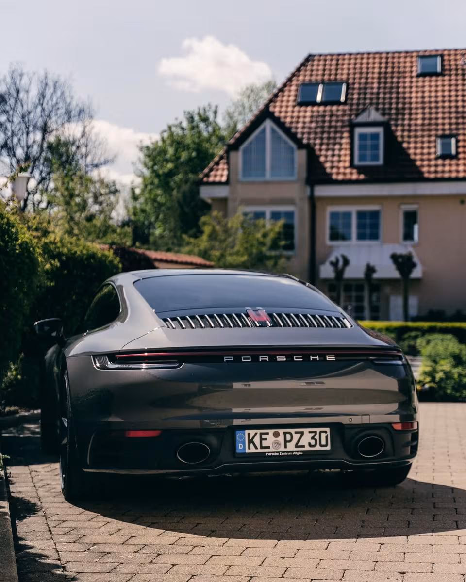 Schwarzer Porsche 911 Carrera 4S von hinten vor einem Einfamilienhaus.