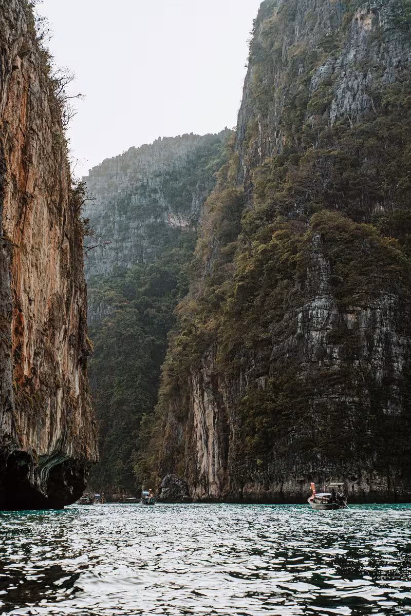 Thailand: Boote fahren durch eine schmale Bucht mit steilen, bewaldeten Kalkfelsen.