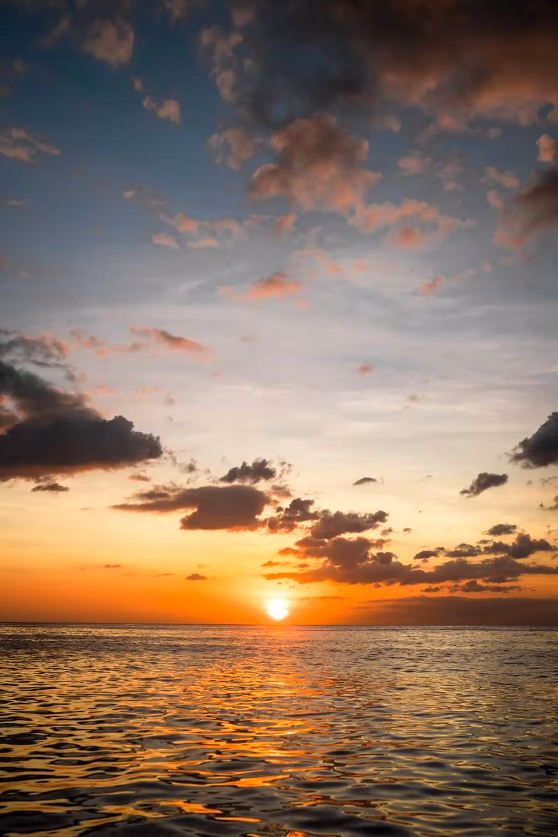 Thailand: Sonnenuntergang über dem Meer mit goldenem Licht und dunklen Wolken
