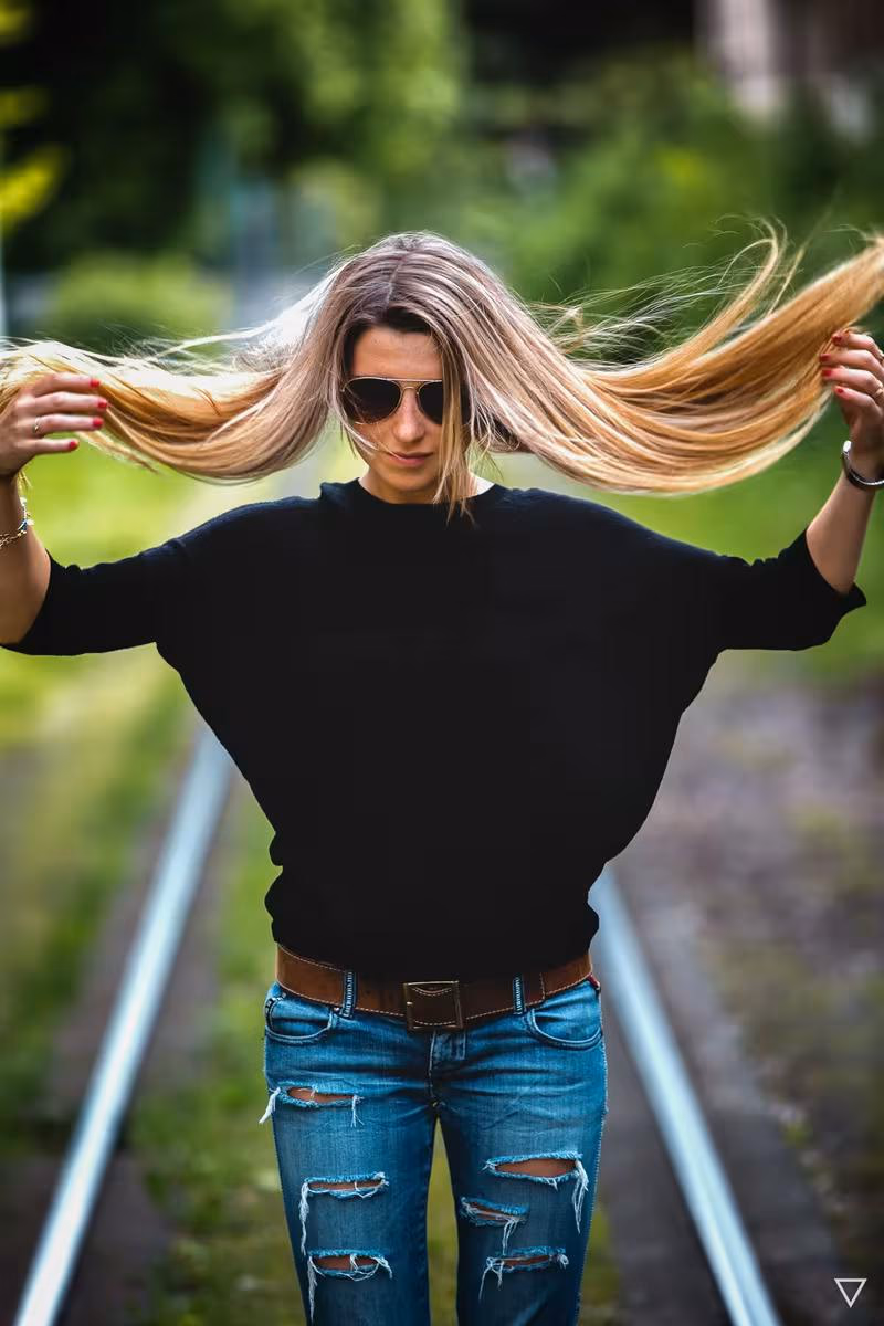 Lifestyle: Frau mit Sonnenbrille und zerfetzten Jeans wirft ihr blondes Haar auf Gleisen.